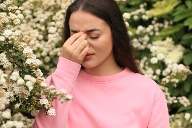 Woman suffering from seasonal pollen allergy near blossoming tree on spring day