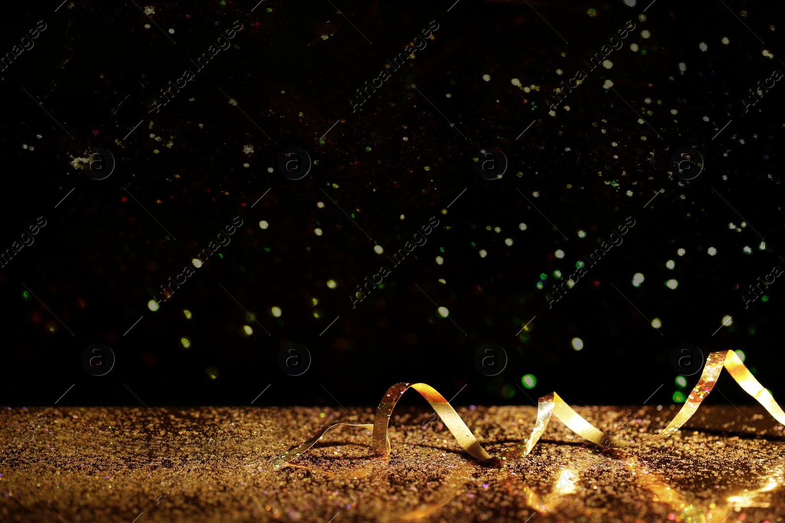Photo of Golden glitter and streamer against black background. Space for text