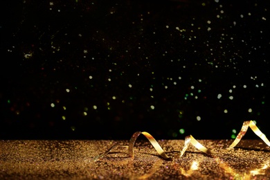 Golden glitter and streamer against black background. Space for text