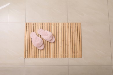 Photo of Wooden mat and slippers on tiled floor, top view. Bathroom accessory