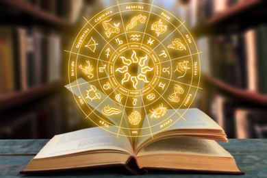 Image of Old book on table indoors and illustration of zodiac wheel with astrological signs
