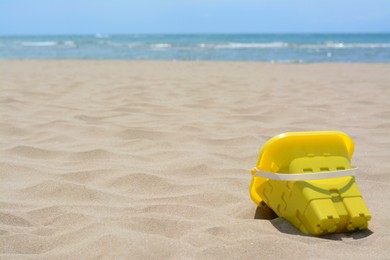 Photo of Yellow plastic bucket on sand near sea, space for text. Beach toy