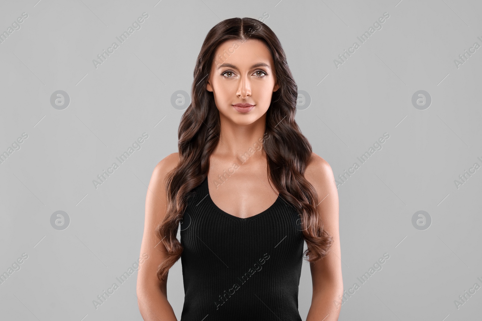 Photo of Hair styling. Portrait of beautiful woman with wavy long hair on grey background