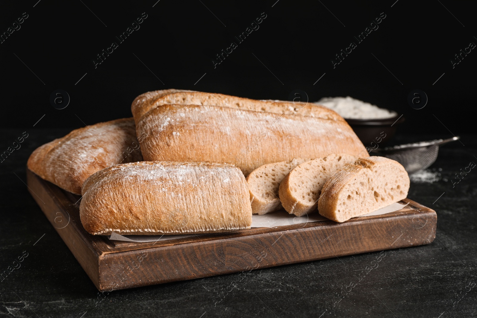 Photo of Wooden board with delicious ciabattas on black table