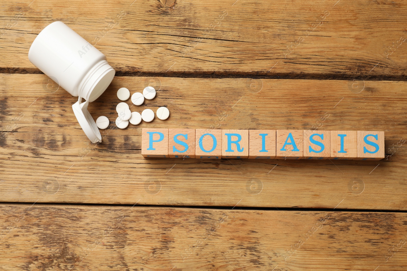 Photo of Word Psoriasis made of cubes with letters and pills on wooden table, flat lay