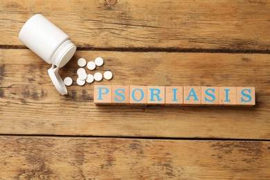 Photo of Word Psoriasis made of cubes with letters and pills on wooden table, flat lay