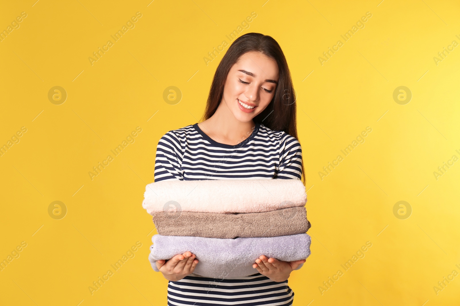 Photo of Happy young woman holding clean laundry on color background