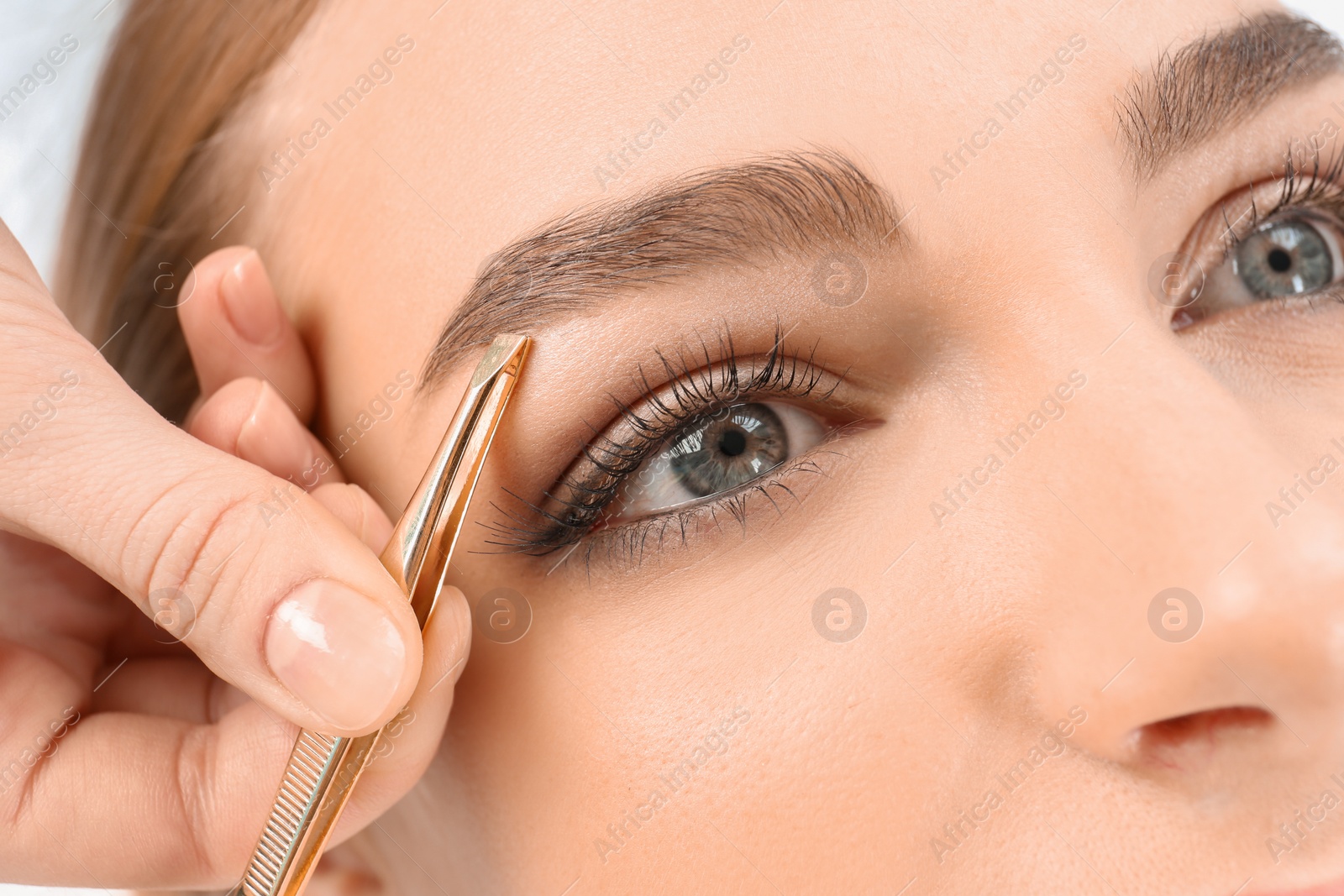 Photo of Young woman having professional eyebrow correction procedure in beauty salon