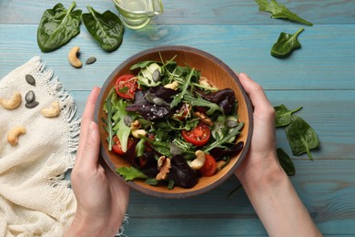 Photo of Woman with tasty fresh vegetarian salad at light blue wooden table, top view