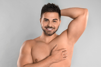 Photo of Young man showing hairless armpit after epilation procedure on grey background