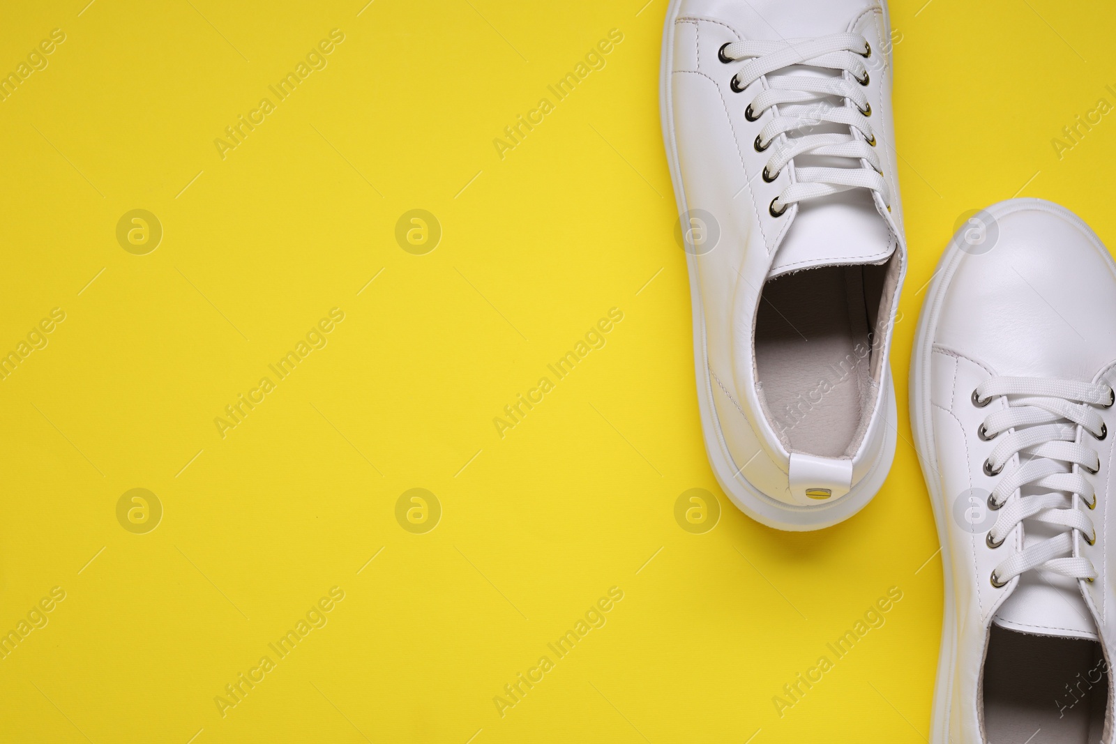 Photo of Pair of stylish white sneakers on yellow background, top view. Space for text