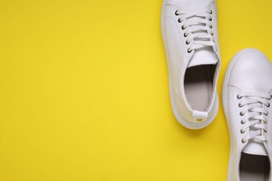 Photo of Pair of stylish white sneakers on yellow background, top view. Space for text