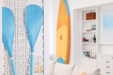 Photo of SUP board and shelving unit with different decor elements in room, focus on paddles, space for text. Stylish interior