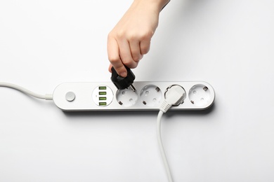 Woman pressing power button of extension cord on white background, top view. Electrician's equipment