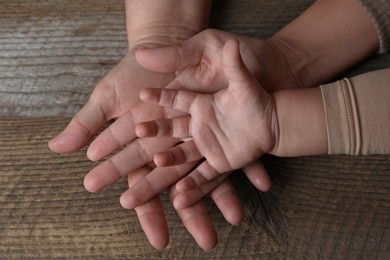 Photo of Family holding hands together at wooden table, top view
