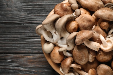 Photo of Different fresh wild mushrooms in bowl on wooden background, top view