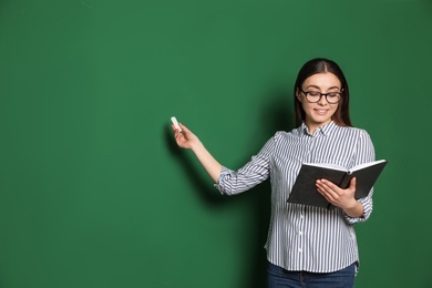 Portrait of young teacher with book and chalk on green background. Space for text