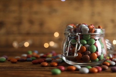 Photo of Delicious dragee in jar on wooden table, closeup. Space for text