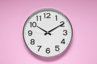 Stylish round clock on pale pink background, top view. Interior element