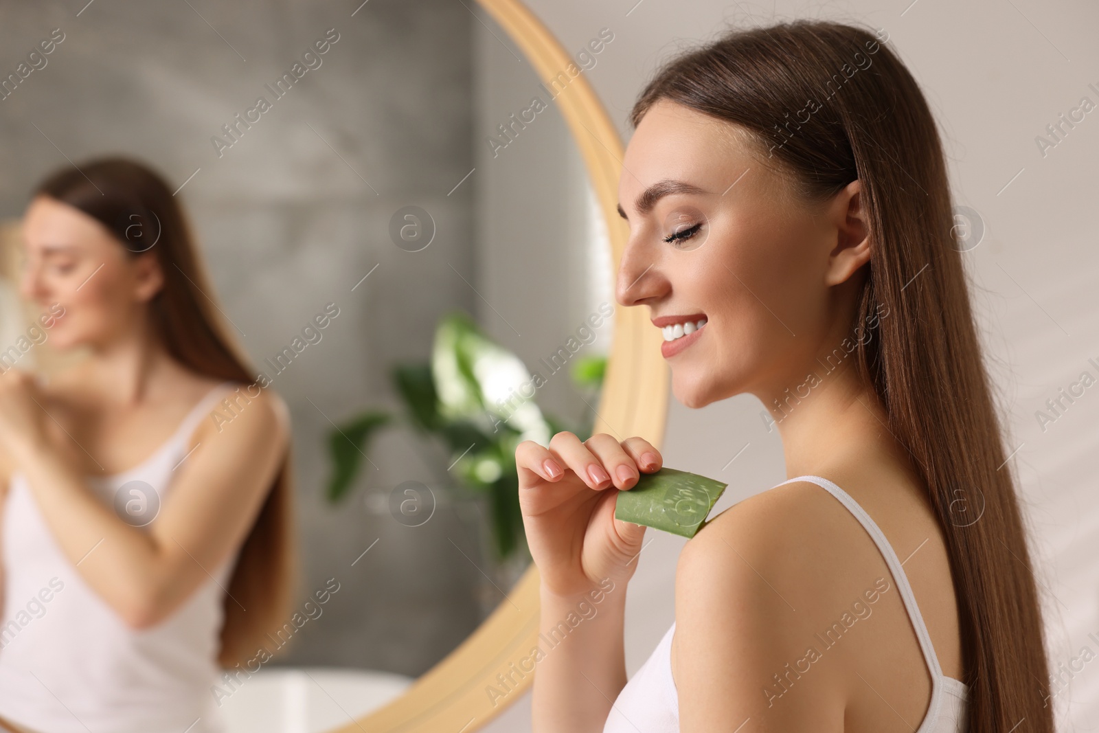 Photo of Young woman applying aloe gel from leaf onto her shoulder in bathroom. Space for text