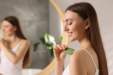 Photo of Young woman applying aloe gel from leaf onto her shoulder in bathroom. Space for text