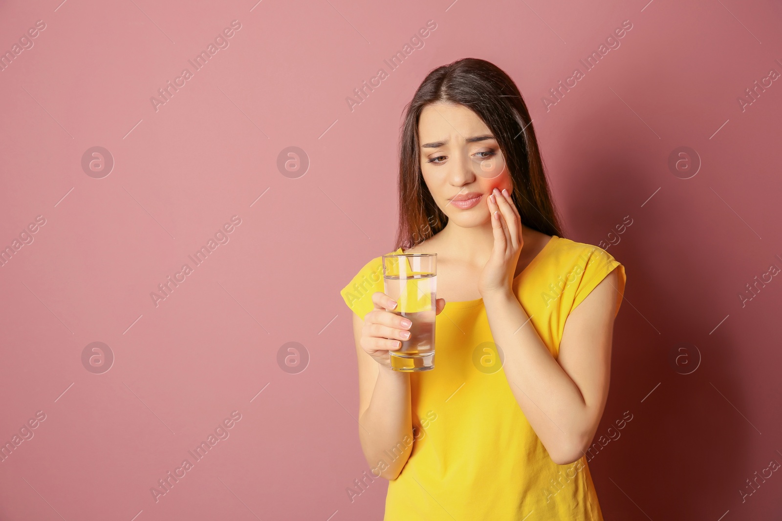 Photo of Woman with sensitive teeth holding glass of water on color background