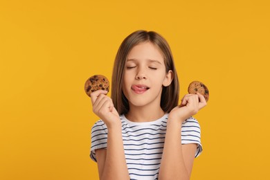Cute girl with chocolate chip cookies showing tongue on orange background