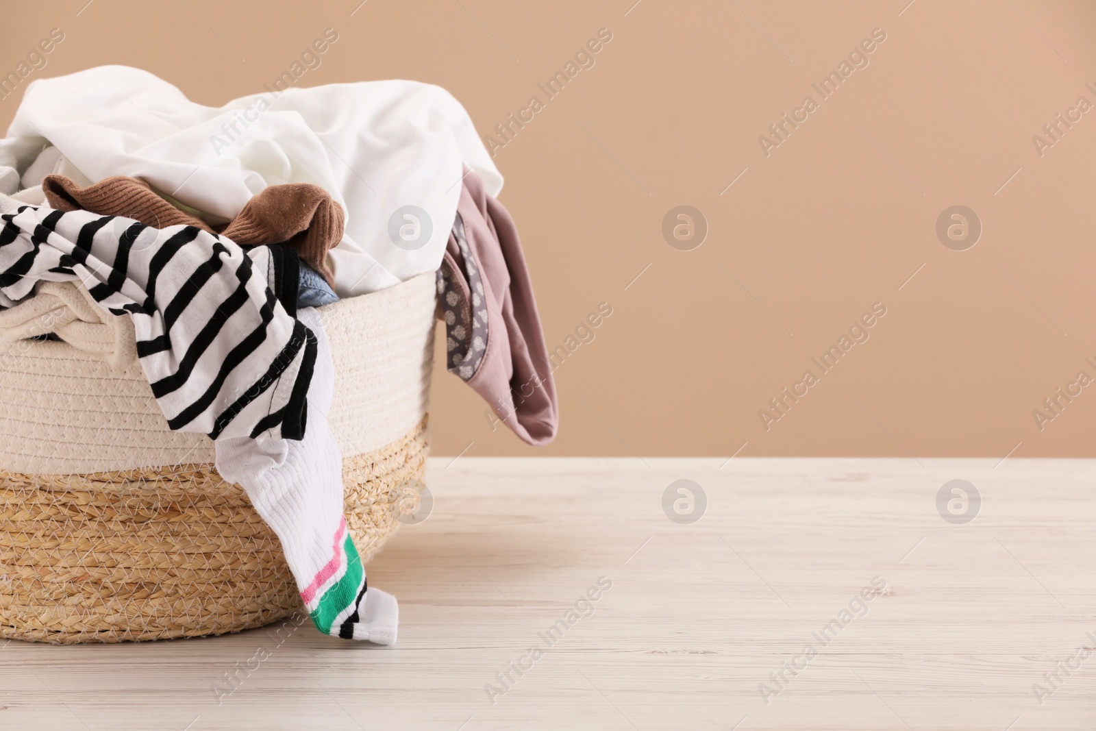 Photo of Wicker laundry basket with clothes near beige wall. Space for text