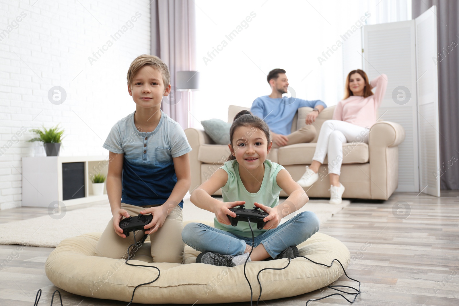 Photo of Cute children playing video games while parents resting on sofa at home