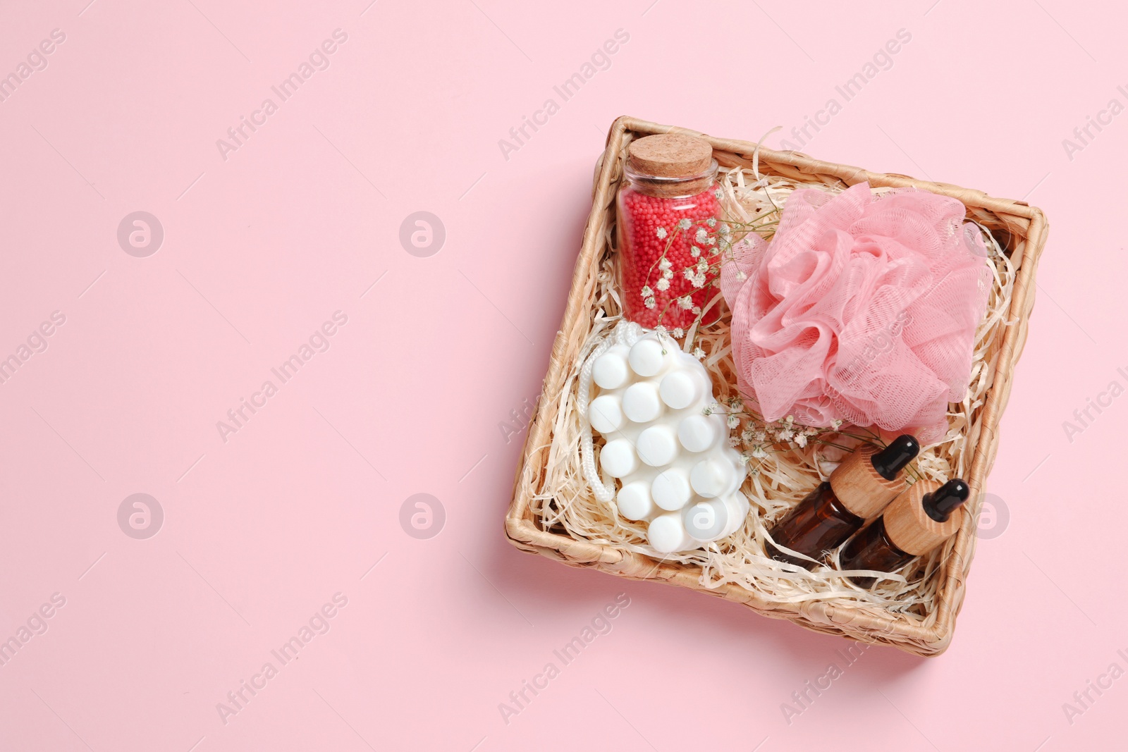 Photo of Spa gift set of different luxury products in wicker basket on pale pink background, top view. Space for text