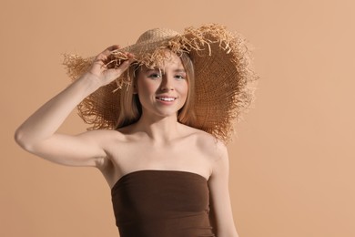 Beautiful young woman in straw hat on beige background