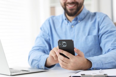 Young man using smartphone at white table in office, closeup