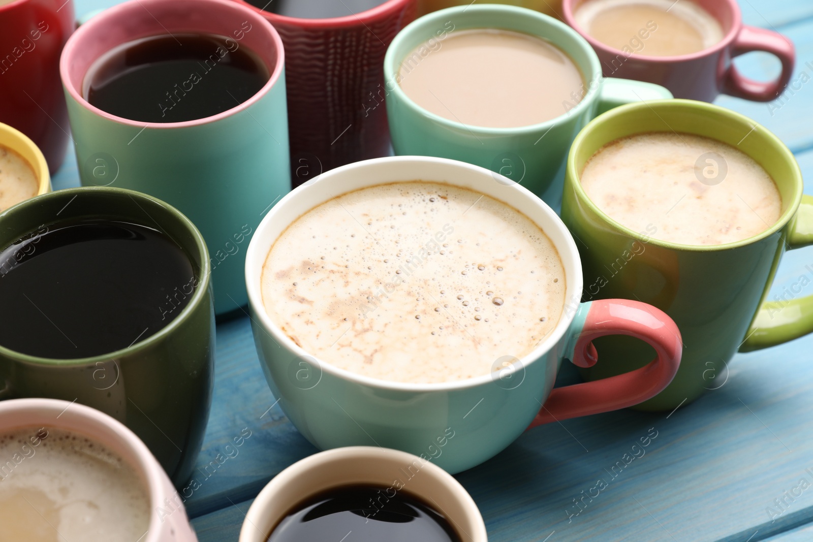 Photo of Many cups of different coffee drinks on light blue wooden table