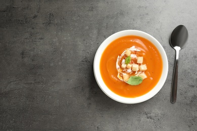 Photo of Bowl of tasty sweet potato soup and spoon on table, top view. Space for text