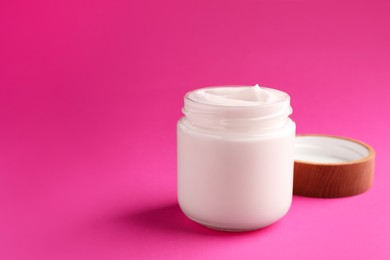 Photo of Glass jar of face cream on pink background. Space for text