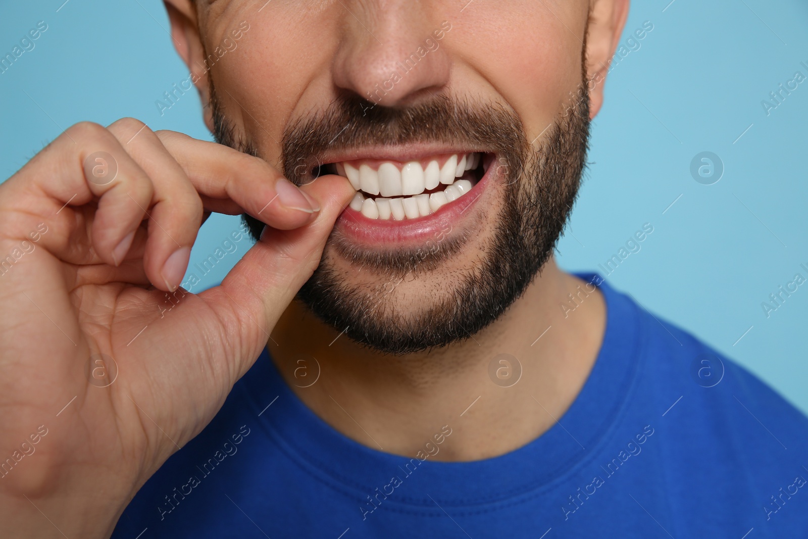 Photo of Man biting his nails on light blue background, closeup