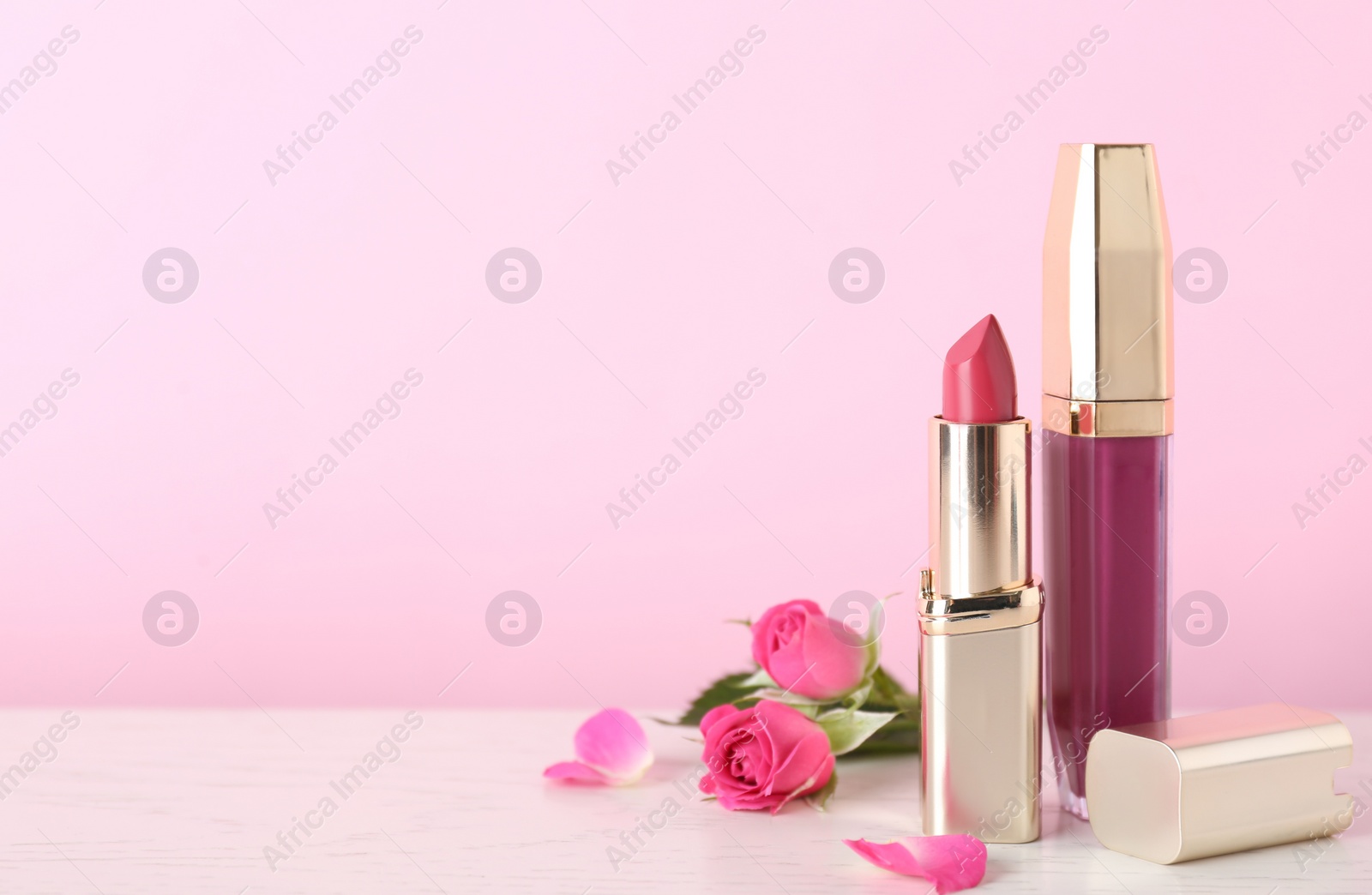 Photo of Lipstick and lip gloss with flowers on table, space for text