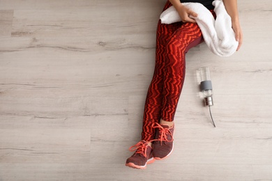 Woman in sportswear with bottle of water and towel sitting on floor indoors, top view. Space for text