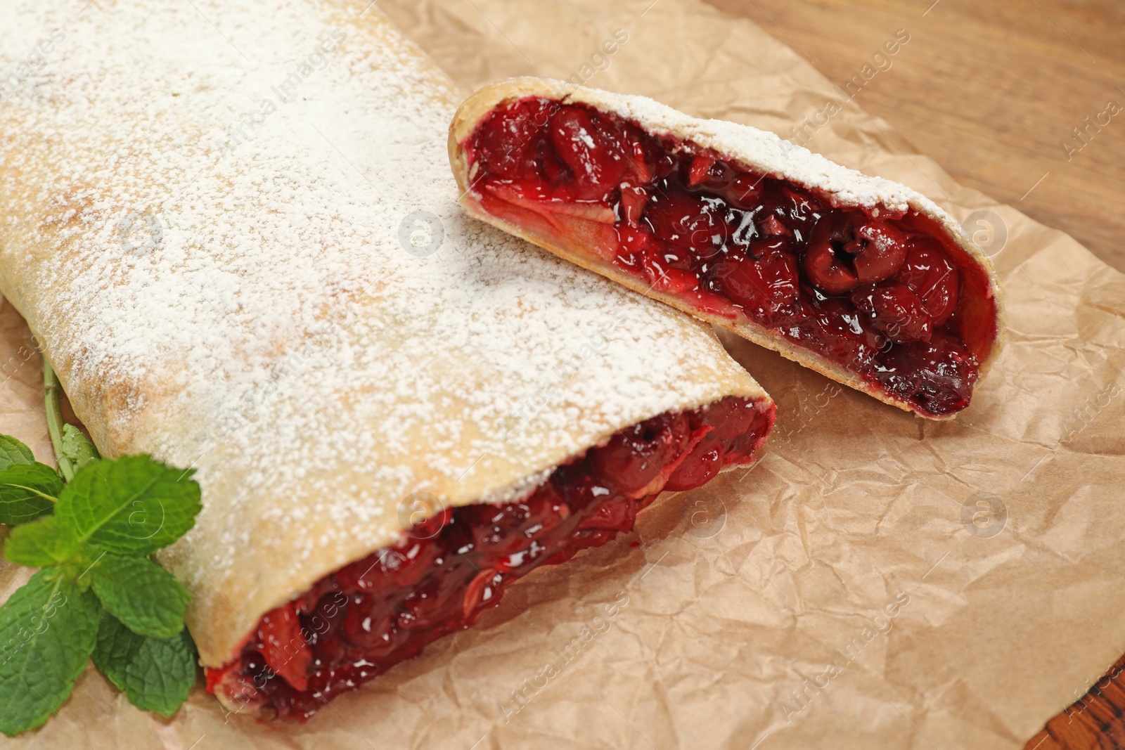 Photo of Delicious strudel with cherries, powdered sugar and mint on parchment paper, closeup