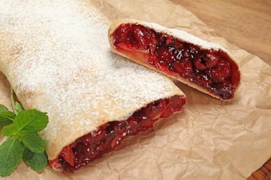 Delicious strudel with cherries, powdered sugar and mint on parchment paper, closeup