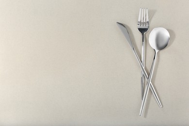 Spoon, fork and knife on light grey background, flat lay. Space for text