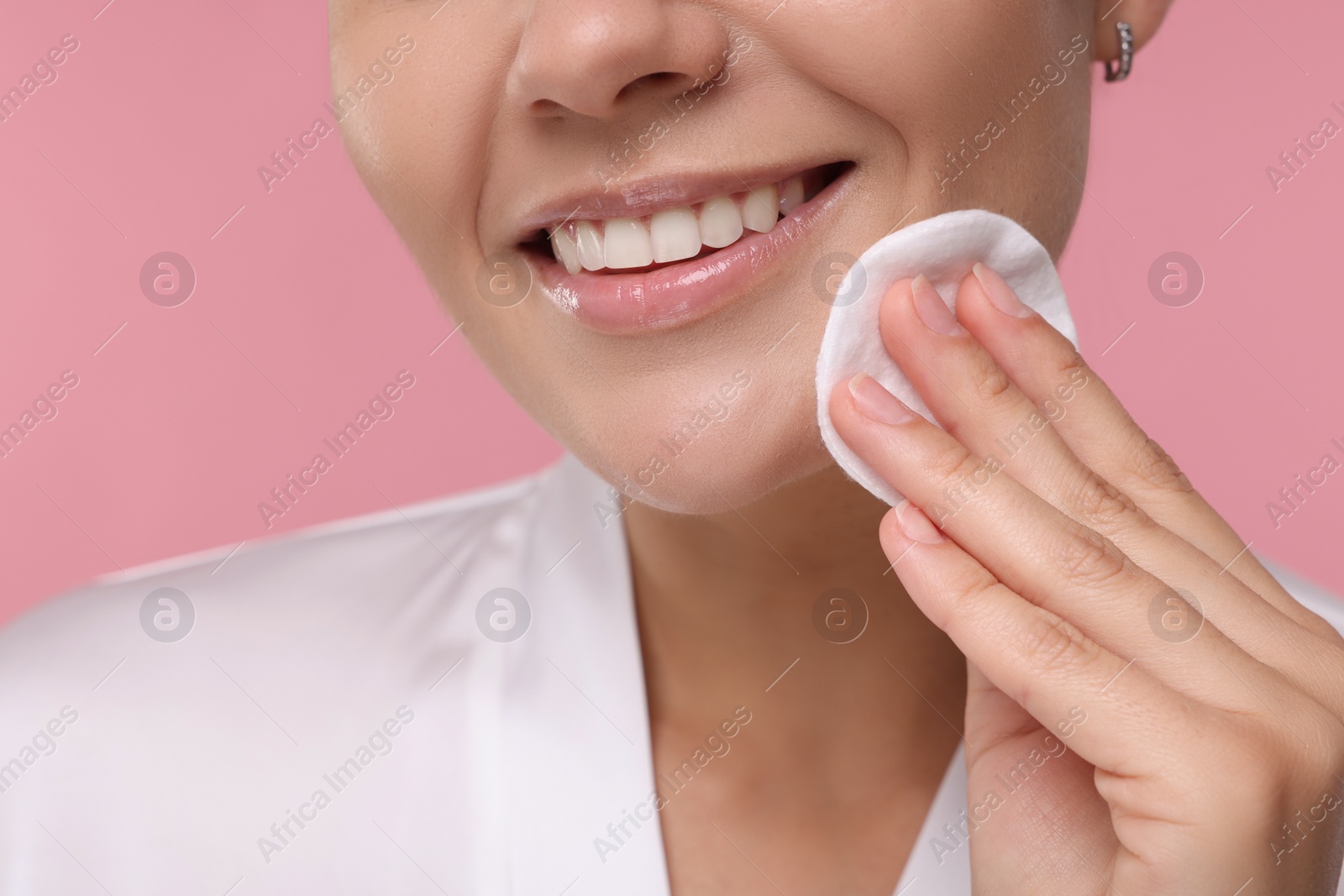 Photo of Young woman cleaning her face with cotton pad on pink background, closeup