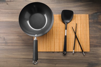 Black metal wok, chopsticks and spatula on wooden table, top view