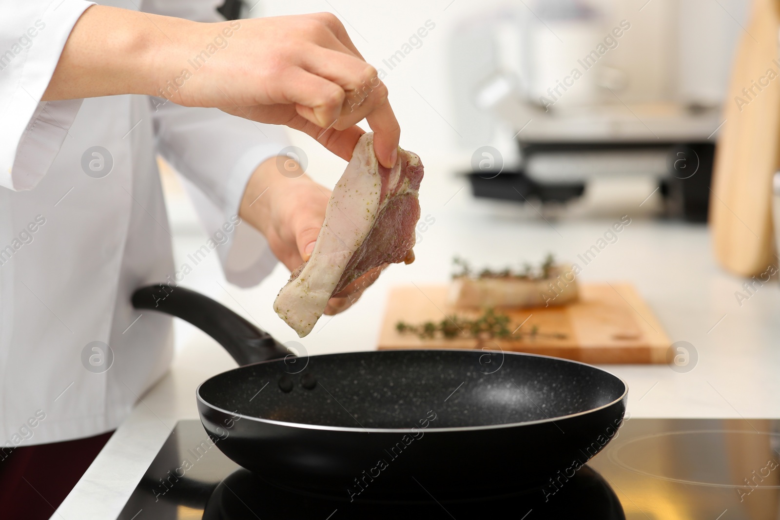 Photo of Professional chef putting fresh meat into frying pan in kitchen, closeup