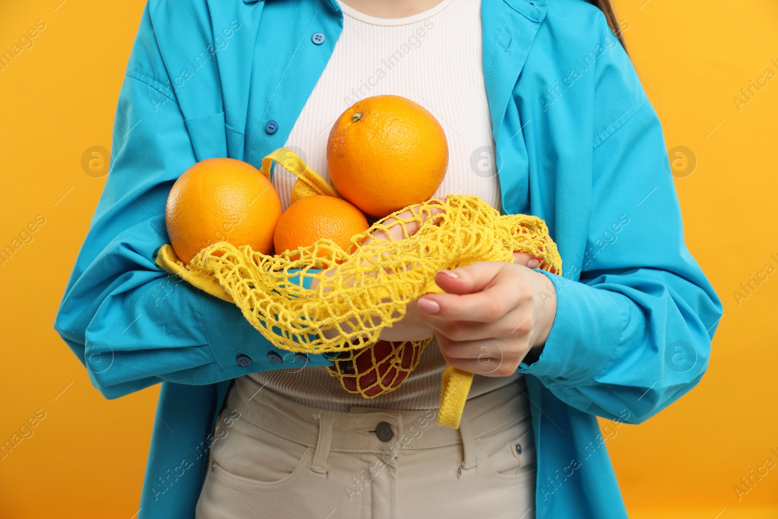 Photo of Woman with string bag of fresh oranges on orange background, closeup