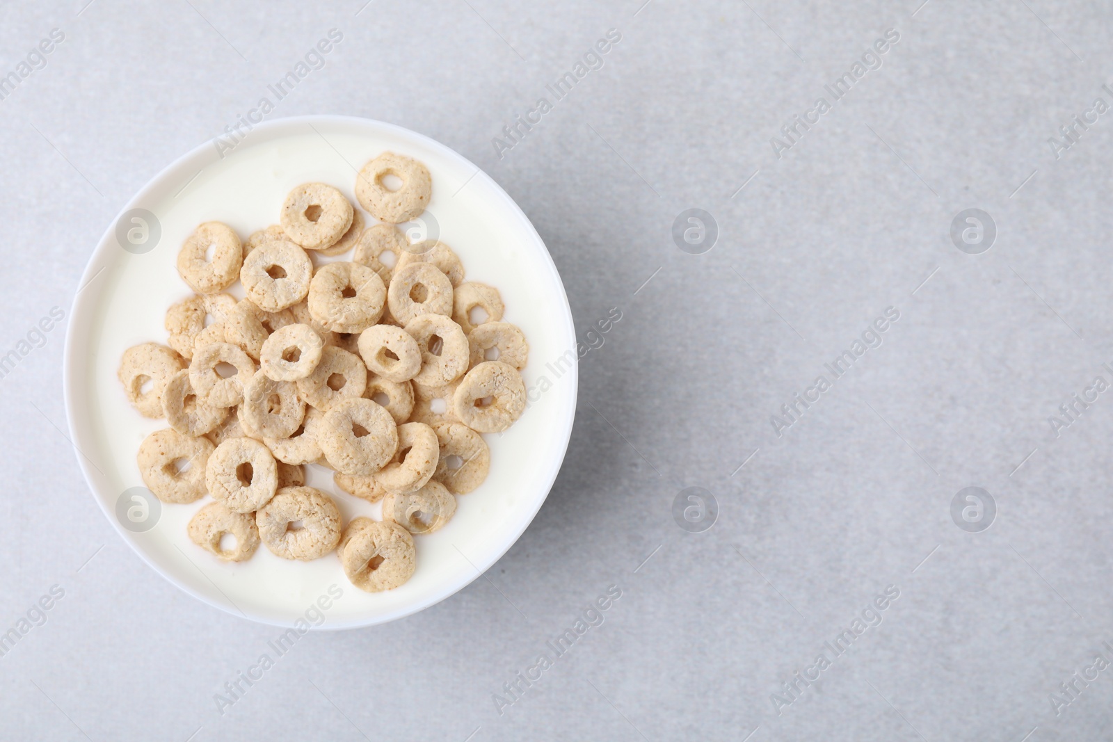 Photo of Breakfast cereal. Tasty corn rings with milk in bowl on grey table, top view and space for text