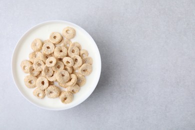 Photo of Breakfast cereal. Tasty corn rings with milk in bowl on grey table, top view and space for text