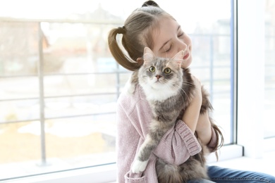 Cute little girl with cat near window at home