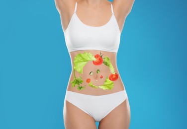 Image of Slim young woman and images of vegetables on her belly against light blue background. Healthy eating