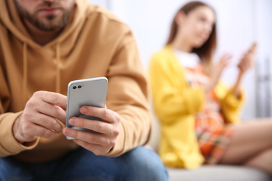Photo of Man with smartphone ignoring his girlfriend at home, closeup. Relationship problems